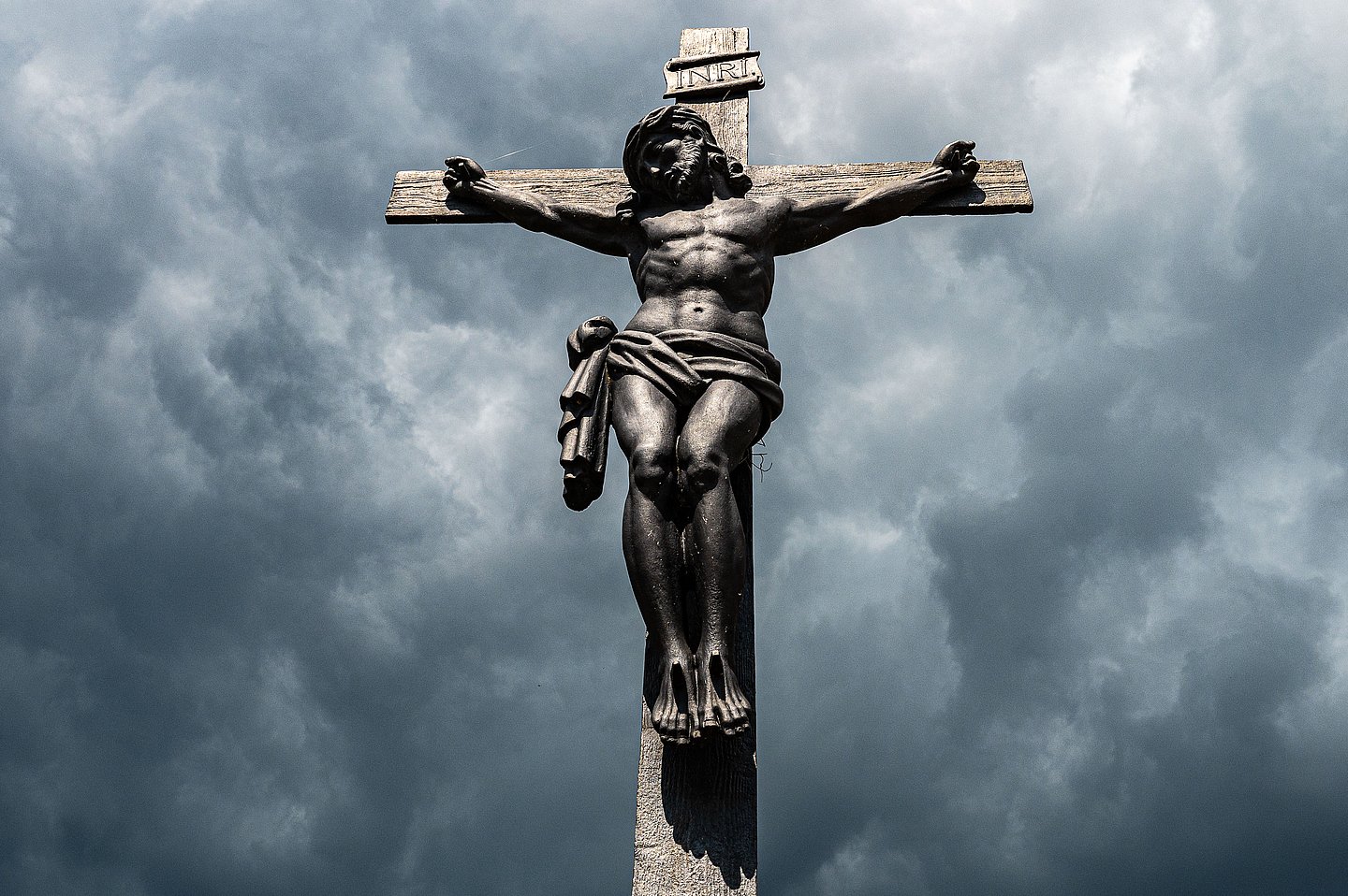 Vor Gewitterwolkenverhangenem Himmel steht das Kruzifix mit dem gekreuzigten Jesus.